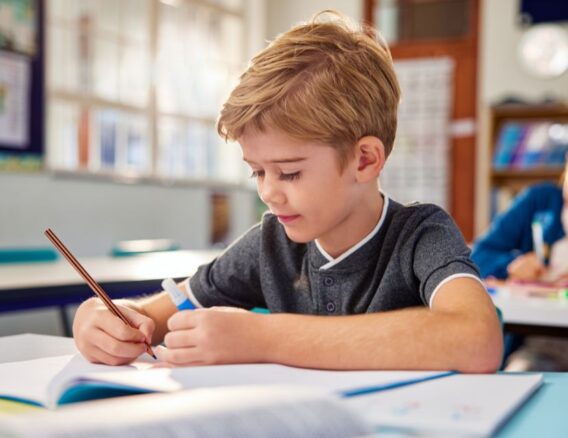 Jongen schrijft in een schrift in een klaslokaal.