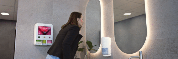 Vrouw in toiletruimte met menstruatie dispenser Tork